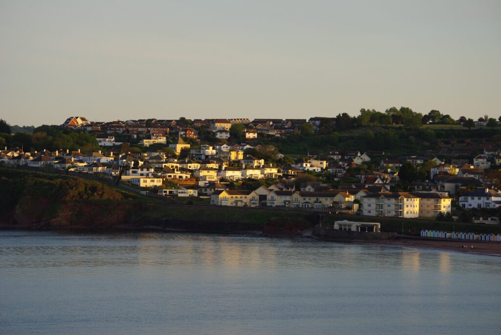 Coastal town with homes overlooking the bay at sunset, showcasing a picturesque seaside community, waterfront properties and scenic coastline in South West England.